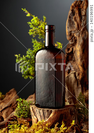 Dark glass vintage bottle of gin or herbal bitter, set among juniper branches, weathered driftwood and forest moss. Dark glass vintage bottle of gin or herbal bitter, set among juniper branches, weathered driftwood and forest moss. 140196991