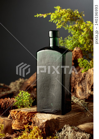 Dark glass vintage bottle of gin or herbal bitter, set among juniper branches, weathered driftwood and forest moss. Dark glass vintage bottle of gin or herbal bitter, set among juniper branches, weathered driftwood and forest moss. 140196993