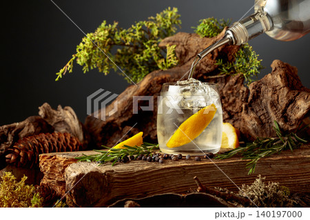 Gin is poured from a bottle into a glass with ice and lemon slice. Gin is poured from a bottle into a glass with ice and lemon slice. 140197000