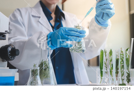 Scientists in lab coats work with plants in a modern lab, focusing on research and experimentation under bright, sterile conditions. 140197154