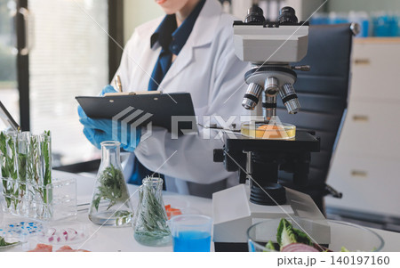Scientists in lab coats work with plants in a modern lab, focusing on research and experimentation under bright, sterile conditions. Scientists in lab coats work with plants in a modern lab, focusing on research and experimentation under bright, sterile conditions. 140197160
