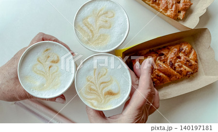 Top view of hands holding takeaway latte art coffees with sweet danish pastries on white table Top view of hands holding takeaway latte art coffees with sweet danish pastries on white table 140197181