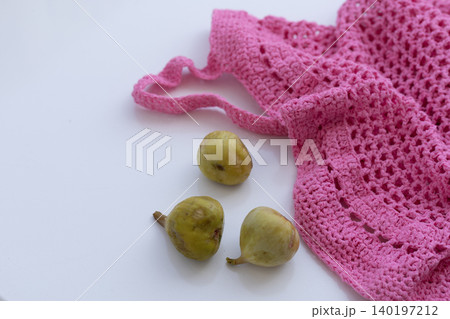Green Figs Next to Pink Crochet Mesh Bag on White Background Green Figs Next to Pink Crochet Mesh Bag on White Background 140197212