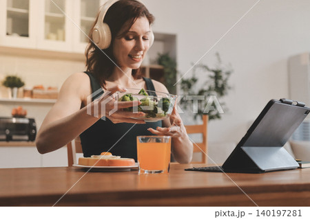 Woman preparing green smoothie in bright kitchen with fresh fruits and vegetables, healthy eating lifestyle moment in natural daylight 140197281