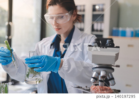 Scientists in lab coats work with plants in a modern lab, focusing on research and experimentation under bright, sterile conditions. Scientists in lab coats work with plants in a modern lab, focusing on research and experimentation under bright, sterile conditions. 140197295