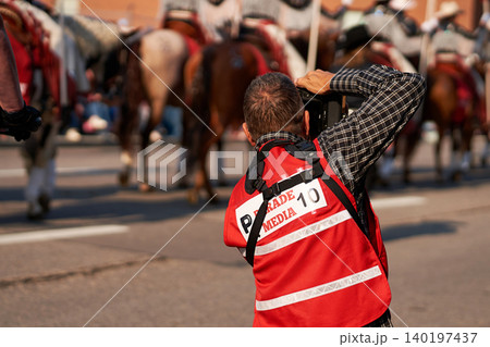 A media photographer in a red press vest taking pictures of a horse procession during the Calgary Stampede Parade. A media photographer in a red press vest taking pictures of a horse procession during the Calgary Stampede Parade. 140197437