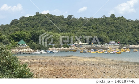Scenic coastal view with a lush green hill, boats, and recreational watercraft Scenic coastal view with a lush green hill, boats, and recreational watercraft 140197446