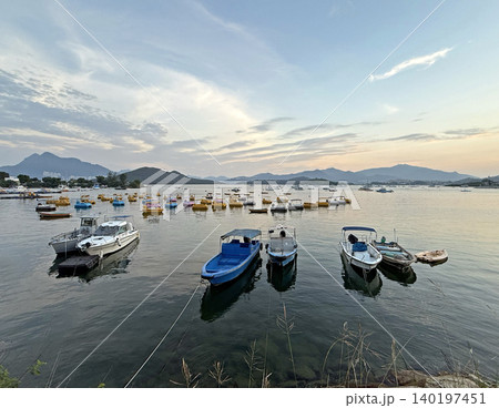 Boats docked in a calm coean at sunset with distant mountains and colorful paddle boats 140197451
