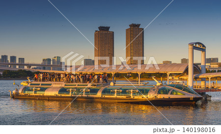 Tokyo, Japan - Oct 13 2024, Panoramic view of Hotaluna water bus filled with passengers sailing along bay, on background of a sharp odaiba with two identical skyscrapers, in evening, Tokyo, Japan Tokyo, Japan - Oct 13 2024, Panoramic view of Hotaluna water bus filled with passengers sailing along bay, on background of a sharp odaiba with two identical skyscrapers, in evening, Tokyo, Japan 140198016