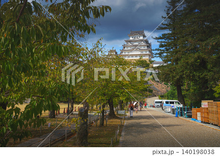 Himeji, Japan - Sep 24 2024, panoramic view of road surrounded by trees and people in distance, in background of Himeji Castle, White Heron Castle, at daytime with cloudy sky, Himeji, Japan Himeji, Japan - Sep 24 2024, panoramic view of road surrounded by trees and people in distance, in background of Himeji Castle, White Heron Castle, at daytime with cloudy sky, Himeji, Japan 140198038