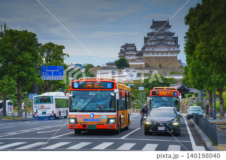 Himeji, Japan - Sep 24 2024, panoramic view of a street with pedestrian crossing, trees, cars, buses and a motorcyclist, in background Himeji Castle, White Heron Castle, on a cloudy day, Himeji, Japan Himeji, Japan - Sep 24 2024, panoramic view of a street with pedestrian crossing, trees, cars, buses and a motorcyclist, in background Himeji Castle, White Heron Castle, on a cloudy day, Himeji, Japan 140198040
