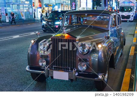 Tokyo, Japan - Oct 15 2024, A close-up view of a vintage Rolls-Royce Silver Cloud car parked at curb in central Tokyo, with people walking in background and cars speeding along road, Tokyo, Japan Tokyo, Japan - Oct 15 2024, A close-up view of a vintage Rolls-Royce Silver Cloud car parked at curb in central Tokyo, with people walking in background and cars speeding along road, Tokyo, Japan 140198209