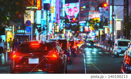 Tokyo, Japan - Oct 15 2024, panoramic view of many cars standing in traffic, on a street at night, on facades of buildings are many bright signs, people walking along, Shibuya Crossing, Tokyo, Japan 140198213