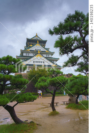 Osaka, Japan - Sep 22 2024, Panoramic view of Osaka Castle among the trees, from behind the fortress wall and the foliage of the trees, on a rainy day, without people, Osaka, Japan 140198235