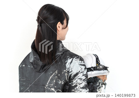 ペンキ汚れの作業着を着てヘルメットを持つ笑顔の若い女性作業員 白背景 ペンキ汚れの作業着を着てヘルメットを持つ笑顔の若い女性作業員 白背景 140199873