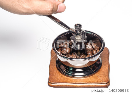 a hand holding handle of the grinding machine  coffee with coffee beans from on white background 140200958