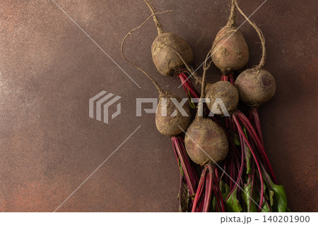 Beets with green leaves rest on a brown surface in a kitchen. The setting is warm and hints at fresh produce ready for cooking or eating Beets with green leaves rest on a brown surface in a kitchen. The setting is warm and hints at fresh produce ready for cooking or eating 140201900