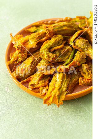 Crispy deep-fried zucchini flowers are displayed on a vibrant plate, showcasing their golden texture. Perfect for sharing during a summer gathering or family meal 140201951