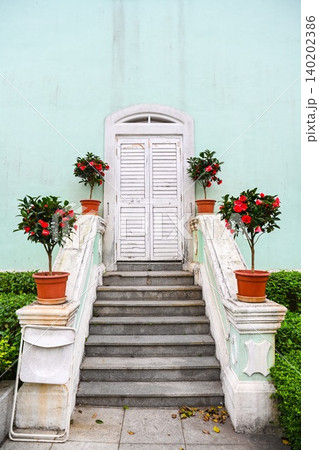 Vertical symmetrical view of white wooden shutter door on mint green facade with camellia flowerpots built in 1921 at Taipa Houses museum Macau Vertical symmetrical view of white wooden shutter door on mint green facade with camellia flowerpots built in 1921 at Taipa Houses museum Macau 140202386