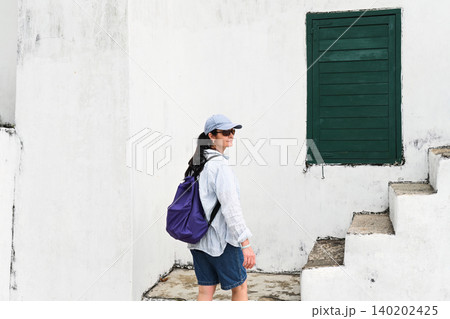 Profile of mature 50 years old Russian woman tourist in cap with backpack near ancient stairs and green window at Guia Lighthouse in Macau China Profile of mature 50 years old Russian woman tourist in cap with backpack near ancient stairs and green window at Guia Lighthouse in Macau China 140202425