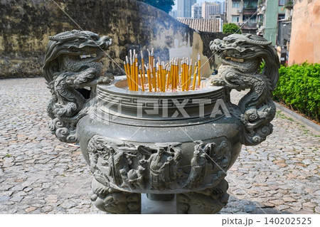 Traditional Chinese stone incense burner with carved dragon sculpture and burning joss sticks at historical temple in Macau landmark China 140202525