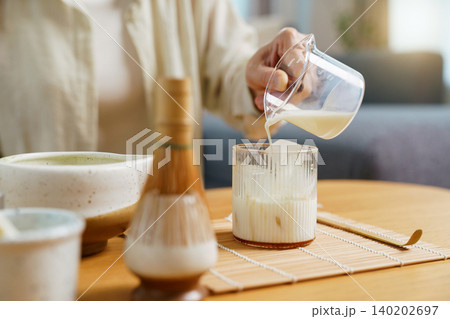 Woman pouring milk into iced glass to make matcha latte 140202697