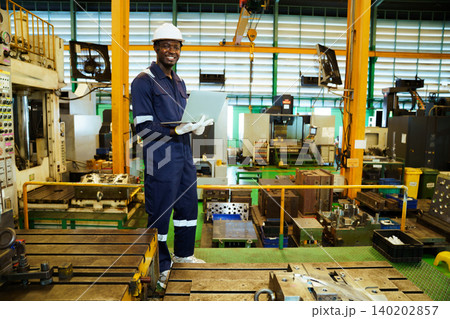 Professional engineer smiling with laptop in manufacturing plant Professional engineer smiling with laptop in manufacturing plant 140202857