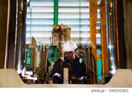 Black engineer using laptop to check machinery in factory Black engineer using laptop to check machinery in factory 140202861