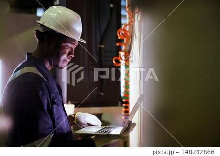 Black engineer using laptop to check machinery in factory Black engineer using laptop to check machinery in factory 140202866
