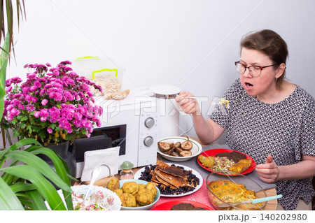 A person sits at a kitchen table eating food. Dishes with different homemade meals are arranged around her. Flowers add color to the table setting. A microwave is nearby A person sits at a kitchen table eating food. Dishes with different homemade meals are arranged around her. Flowers add color to the table setting. A microwave is nearby 140202980
