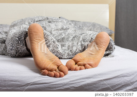 A man is relaxing in bed with his feet sticking out of the covers. He seems to have settled down for the night after a busy day at home or in a hotel room A man is relaxing in bed with his feet sticking out of the covers. He seems to have settled down for the night after a busy day at home or in a hotel room 140203397