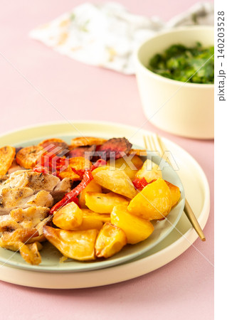 A plate holds baked potato, sliced baked chicken breast, and roasted vegetables like carrots, peppers, and beets. A drink sits nearby with a slice of lime 140203528