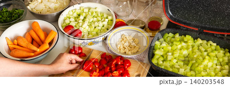 A woman cuts tomatoes on a wooden board surrounded by fresh vegetables while preparing squash caviar for winter canning in her kitchen, banner A woman cuts tomatoes on a wooden board surrounded by fresh vegetables while preparing squash caviar for winter canning in her kitchen, banner 140203548