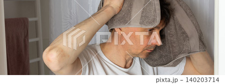 A 53-year-old man stands in the bathroom with a towel over his head while preparing for the day. He is focused on his morning tasks, surrounded by a clean setting, banner A 53-year-old man stands in the bathroom with a towel over his head while preparing for the day. He is focused on his morning tasks, surrounded by a clean setting, banner 140203714