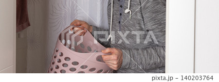 A 53-year-old man takes laundry from the washing machine into a basket in a home laundry area during the afternoon, focused on his task, banner A 53-year-old man takes laundry from the washing machine into a basket in a home laundry area during the afternoon, focused on his task, banner 140203764