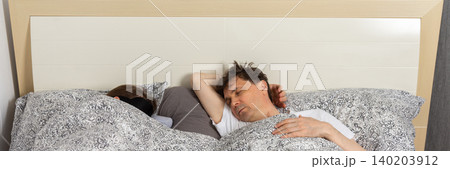 A fifty-year-old couple sleeps side by side in their bedroom at night. They are covered with blankets and resting after a long day, banner A fifty-year-old couple sleeps side by side in their bedroom at night. They are covered with blankets and resting after a long day, banner 140203912