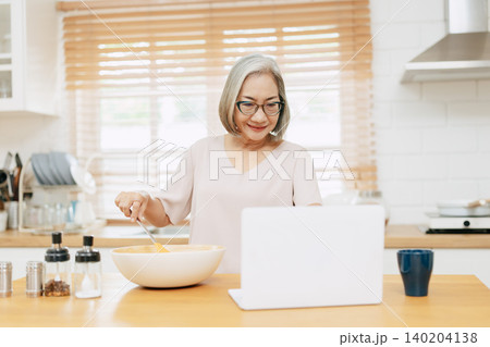 Senior Asian woman using Laptop computer modern technology to learn and live teaching cook kitchen Senior Asian woman using Laptop computer modern technology to learn and live teaching cook kitchen 140204138