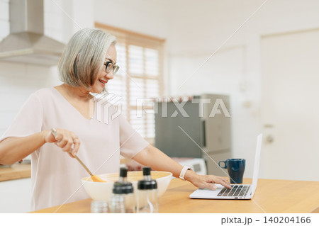 Senior Asian woman using Laptop computer modern technology to learn and live teaching cook kitchen Senior Asian woman using Laptop computer modern technology to learn and live teaching cook kitchen 140204166