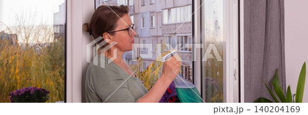 A person is washing windows in an apartment on a balcony filled with flowers. This activity takes place in fall as winter approaches, preparing for the colder months 140204169