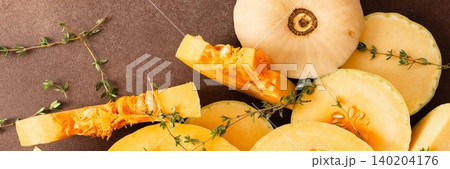 Yellow squash sliced into pieces is placed on a brown surface. Garlic cloves and fresh thyme are nearby, adding texture and color to the arrangement of vegetables, banner Yellow squash sliced into pieces is placed on a brown surface. Garlic cloves and fresh thyme are nearby, adding texture and color to the arrangement of vegetables, banner 140204176