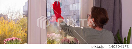 A person cleans windows in a city apartment on a balcony. The scene shows autumn flowers and a clear view outside on a sunny day as winter approaches, banner A person cleans windows in a city apartment on a balcony. The scene shows autumn flowers and a clear view outside on a sunny day as winter approaches, banner 140204178