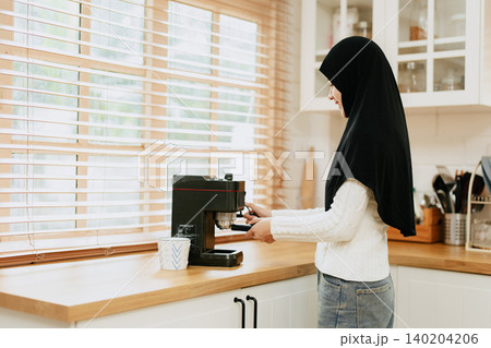Woman in a black hijab make a coffee with espresso machine at home, Arab drinks coffee Woman in a black hijab make a coffee with espresso machine at home, Arab drinks coffee 140204206