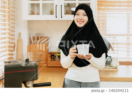 Woman in a black hijab make a coffee with espresso machine at home, Arab drinks coffee Woman in a black hijab make a coffee with espresso machine at home, Arab drinks coffee 140204211