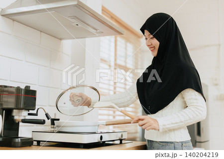 Arab Muslim Young woman cooking food at home kitchen happy smiling Arab Muslim Young woman cooking food at home kitchen happy smiling 140204219