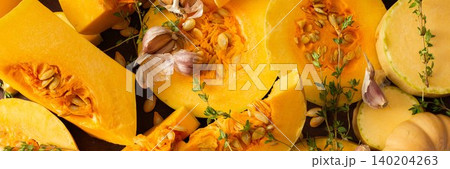 The scene shows various pieces of cut squash placed on a wooden table. Fresh thyme sprigs are scattered among the squash. Natural light fills the area, emphasizing the colors, banner 140204263