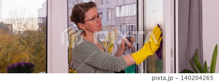 A person is cleaning the windows of an apartment balcony in the fall season. Flowers are present in pots, and the sun is shining on the scene, banner A person is cleaning the windows of an apartment balcony in the fall season. Flowers are present in pots, and the sun is shining on the scene, banner 140204265
