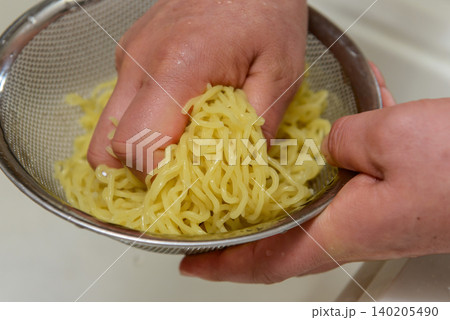 ザルに入れた中華麺を流水で洗って締めるシーン 140205490