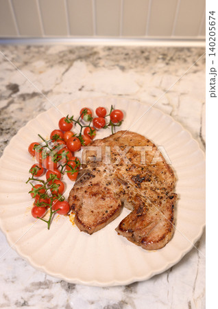 Grilled pork, cherry tomato, white plate, marble counter, home kitchen meal with fresh red vegetable garnish Grilled pork, cherry tomato, white plate, marble counter, home kitchen meal with fresh red vegetable garnish 140205674