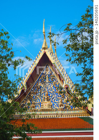 Wat arun temple dawn bangkok chao phraya river ornate gable framed by green tree under vivid blue sky 140205691