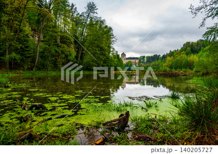 Kost Castle rises above a pond in the Bohemian Paradise region of the Czech Republic. Forests surround the landscape under cloudy skies, creating a scenic historic view. Kost Castle rises above a pond in the Bohemian Paradise region of the Czech Republic. Forests surround the landscape under cloudy skies, creating a scenic historic view. 140205727